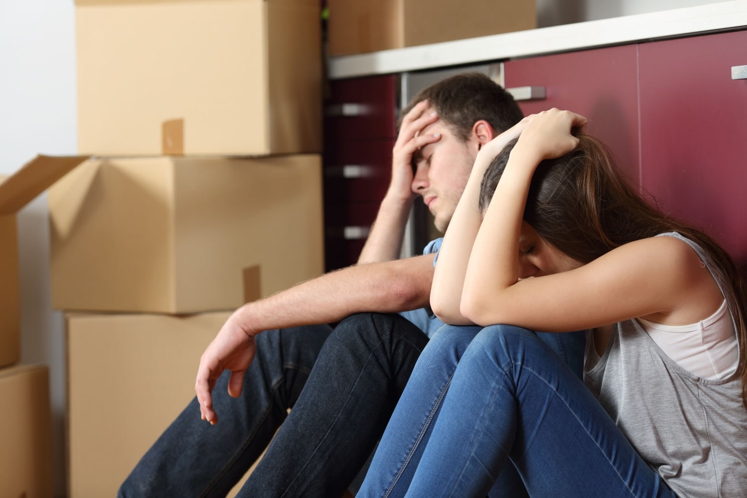 Junges Paar sitzt enttäuscht vor gepackten Umzugskartons in der Wohnung.