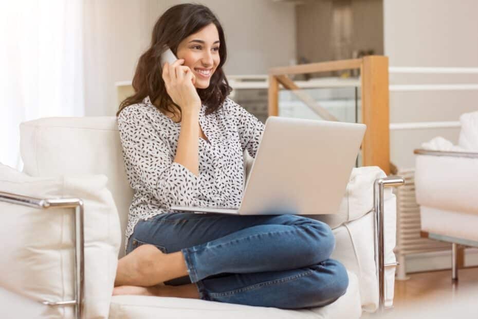 Frau auf einem Sofa, Laptop auf den Knien, Telefon in der Hand