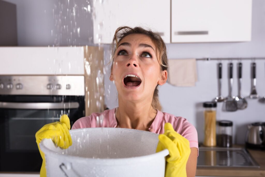 Frau steht in der Küche und hält einen Eimer, während von oben Wasser runterkommt